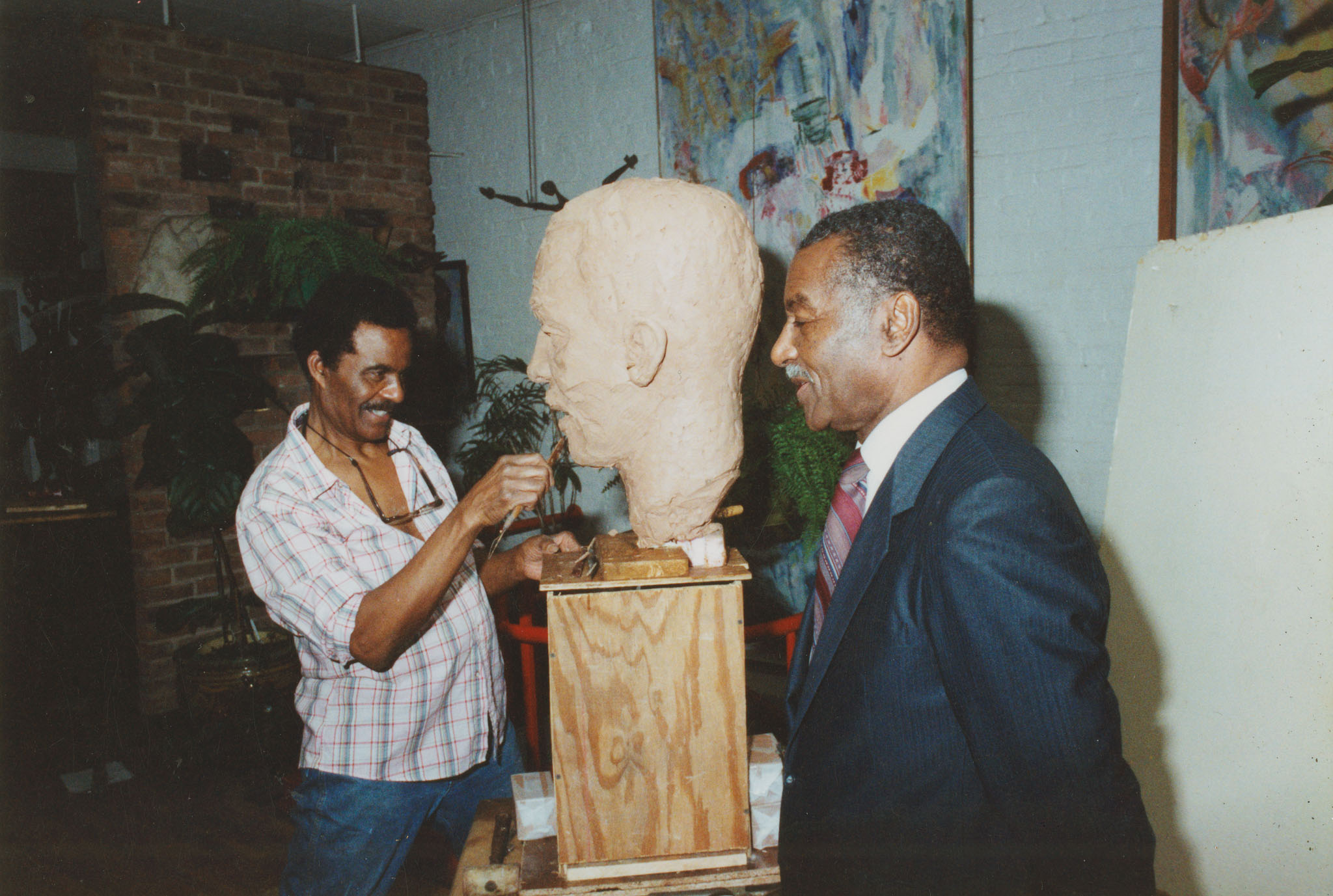 A sculptor working on a bust with a person modeling.