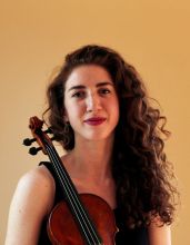 photo of Willa Finck, who is light-skinned with long brown wavy hair and the neck of the violin is resting on the right shoulder.