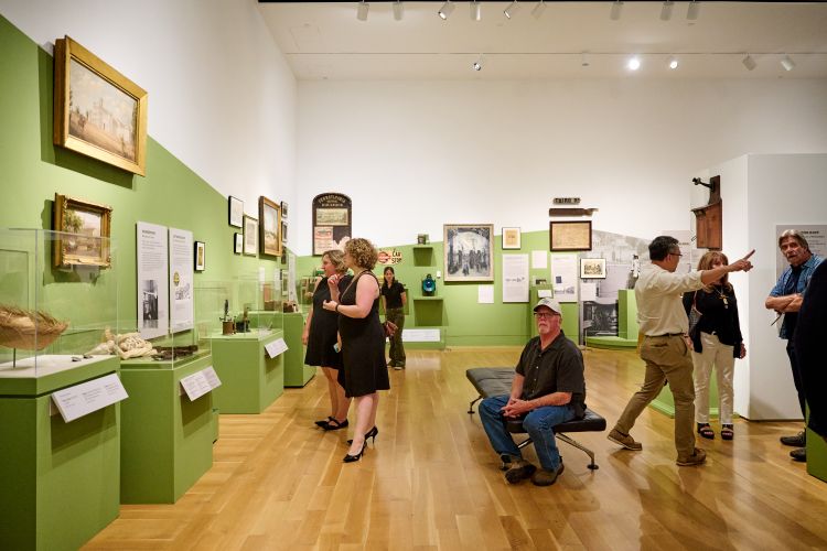 People standing in a gallery featuring historic objects on display.