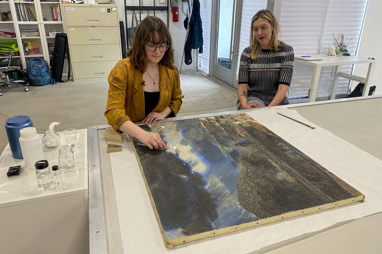 Curator Ali Printz behind a conservator working on Henry Carter's Coal Mine. 