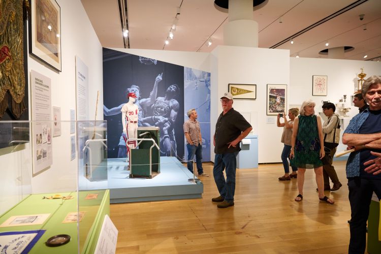 People standing in a gallery featuring historic objects on display.