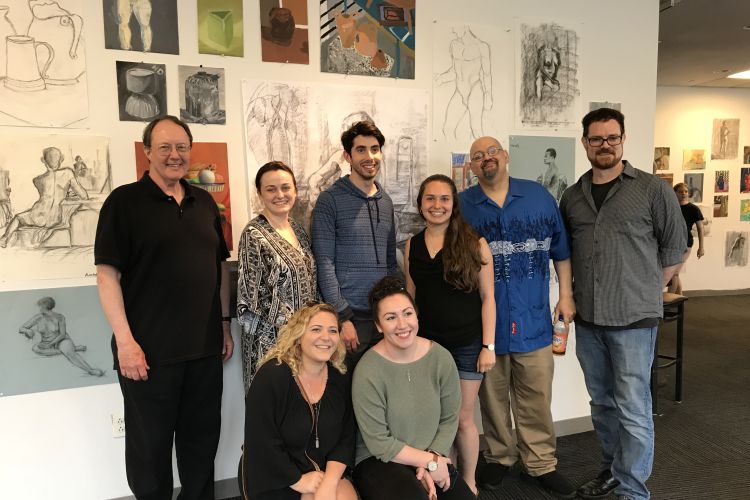 Al Gury posing with a group of students with artwork in the background